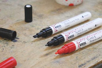 KREUL Glass & Porcelain Pens displayed on a wooden surface showing fine black tip and colored medium tips including red