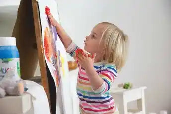 MUCKI Finger Paint white 150 ml jar with colorful children’s artwork in the background.